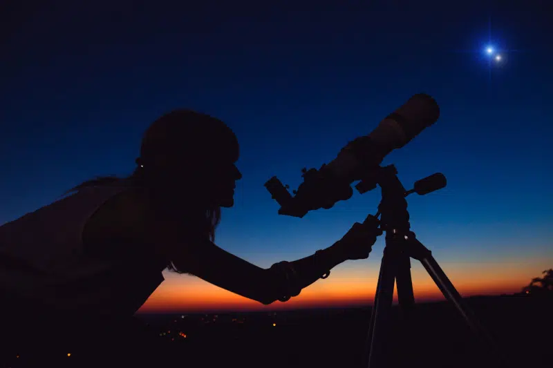 Woman looking at night sky with amateur astronomical telescope.