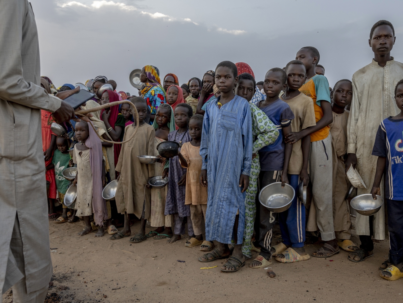  A man with a whip attempted to control a crowd of Sudanese children who were jostling to receive food during an impromptu aid distribution on the outskirts of Adre refugee camp.